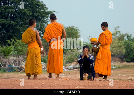 Eine Gruppe buddhistischer Mönche stehen auf einer unbefestigten Straße während des Empfangs Reis von einer Frau in kommunistische Laos. Stockfoto