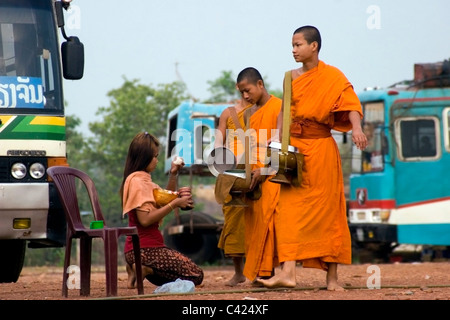 Eine Gruppe buddhistischer Mönche gehen auf einem Feldweg während des Empfangs Reis von einer Frau in kommunistische Laos. Stockfoto