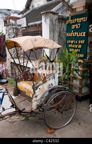 Eine alte verfallene und zerfetzten Rikscha vor einer touristischen Bar auf einem Stadt-Bürgersteig in kommunistische Laos geparkt ist. Stockfoto