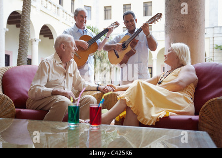 Senior kaukasischen paar sitzt Bar im Hotel und Musiker Gitarre spielen hören. Horizontale Form Stockfoto