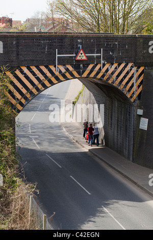 Eisenbahnbrücke über eine Straße. Höhenbeschränkung für underpassing Fahrzeuge. Mutter und Kinder, die durch die unter. North Walsham, Norfolk. Stockfoto