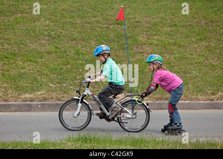 kleiner Junge auf seinem Fahrrad ziehen seine Schwester auf Inline - Skates hinter ihm Stockfoto