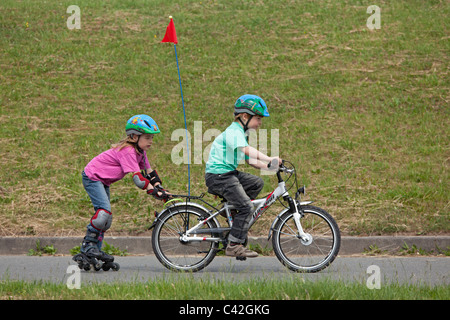 kleiner Junge auf seinem Fahrrad ziehen seine Schwester auf Inline - Skates hinter ihm Stockfoto