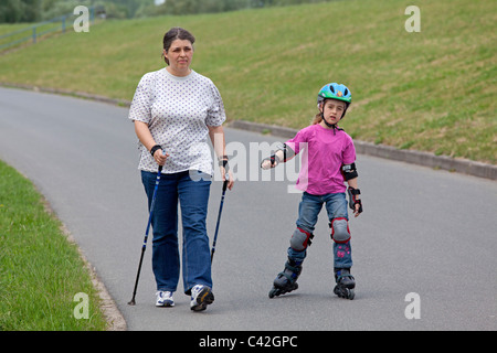 eine Frau mittleren Alters, Nordic Walking, ihrer kleinen Tochter Skaten neben ihr zu tun Stockfoto