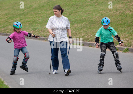 eine Frau mittleren Alters, die ihre zwei kleinen Kinder Skaten neben ihr tun Nordic Walking Stockfoto