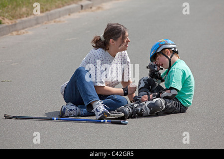 eine Frau mittleren Alters tröstet ihren jungen Sohn, der sich selbst beim Inline-Skaten zu verletzen Stockfoto