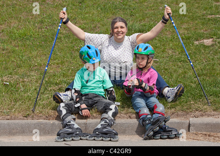 eine Frau mittleren Alters und ihren zwei kleinen Kindern, die eine Pause vom Nordic Walking und Inline-skating Stockfoto