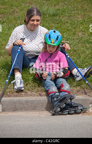 eine Frau mittleren Alters und ihrer kleinen Tochter, die eine Pause vom Nordic Walking und Inline-skating Stockfoto