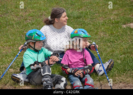 eine Frau mittleren Alters und ihren zwei kleinen Kindern, die eine Pause vom Nordic Walking und Inline-skating Stockfoto