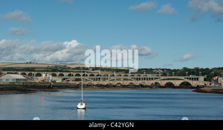Auf dem Fluss Tweed in Berwick, eine Yacht vor Anker in den Vordergrund, Straßen- und Eisenbahnbrücken im Hintergrund. Stockfoto