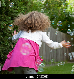 Ein kleines Mädchen spielt in ihrem Garten, um Luftblasen zu fangen versuchen. Stockfoto