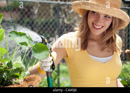 Lächelnde junge Frau Bewässerung Blumen im Garten Stockfoto
