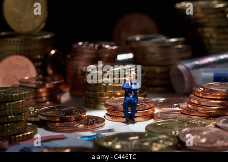 Eine Miniatur Geschäftsmann Figur mit verschränkten Armen sitzt auf einem Stapel von Münzen Stockfoto