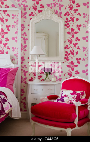 Roter samt Sessel im Schlafzimmer mit Bett Schlafzimmereinrichtungen und Designers Guild Blumentapete rosa Stockfoto