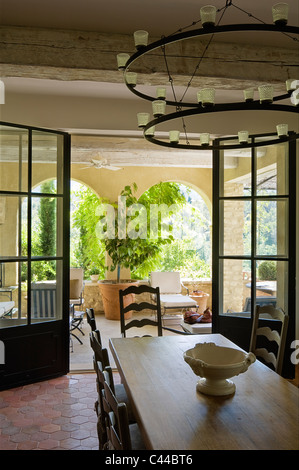 Esstisch aus Holz und Kandelaber in Zimmer mit gefliesten Terrakotta-Böden und durch geöffneten Flügeltüren zur loggia Stockfoto