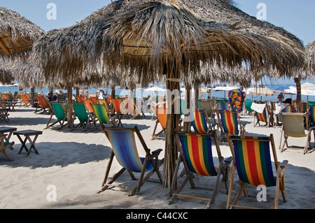 Stühle sind im Schatten Palapas und Sonnenschirme am Strand von Los Muertos Strand in Puerto Vallarta, Mexiko aufgereiht. Stockfoto