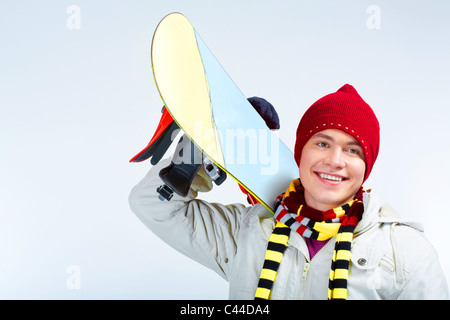 Foto von geschickten Teenager mit Snowboard auf seiner Schulter über blauem Hintergrund Stockfoto