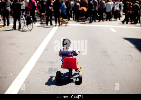 Kind reitet ein Dreirad auf einer Straße hinter Menschen in San Francisco, Kalifornien, während eine monatliche Straße Schließung. Stockfoto