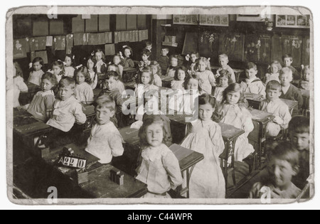 Formale Porträt des Edwardianischen und viktorianischen Säuglinge an Ihrem Schreibtisch in einem strengen Grundschule Klassenzimmer sitzen während einer Lektion mit Kreide auf Schiefer. ca. 1908, U.K. Edwardians, Victorians Stockfoto