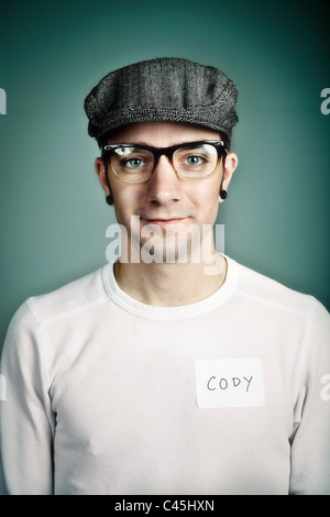 Ein hip und doch freundliche junge Mann trägt eine Mütze und Kunststoff-Gläser mit einem Namensschild. Er hat einen alternativen Look mit geeichte Ohren. Stockfoto