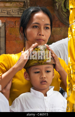 Ein BALINESISCHER junge und seine Mutter ist bei PURA BEJI im Dorf Mas während der GALUNGAN FESTIVAL - UBUD, BALI, Indonesien Stockfoto