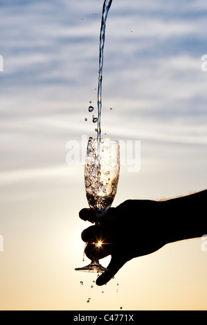 Wasser wird in ein Champagnerglas gegossen. Silhouette Stockfoto