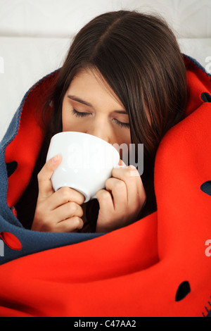 Junge Frau gefangen kalt, eingehüllt in Decke, trinken etwas warmes aus Tasse. Stockfoto