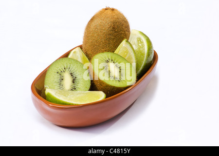 Nahaufnahme von Kiwi und Limette Vierteln in Terrakotta Schale auf weißem Hintergrund Stockfoto