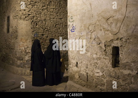 Zwei Frauen tragen traditionelle schwarze Abaya (Hijab) sprechen in der Nacht in der alten Stadt von Sana'a, Jemen. Stockfoto