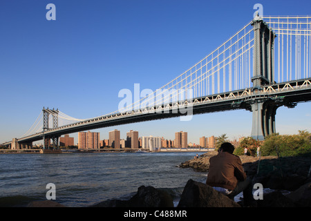 Ein junger Mann sitzt auf einem Felsen am Strand von den East River, New York City, USA Stockfoto