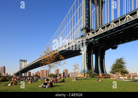 Menschen liegen auf dem Rasen unter der Manhattan Bridge, New York City, USA Stockfoto