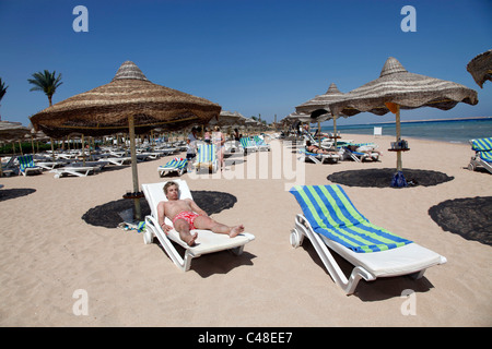 Modell veröffentlicht Mann auf Sommerurlaub und Sonnenbaden auf einer Sonnenliege am Strand mit Sonnenschirme und Großschirme Stockfoto