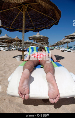 Modell veröffentlicht Mann auf Sommerurlaub und Sonnenbaden auf einer Sonnenliege am Strand mit Sonnenschirme und Großschirme Stockfoto