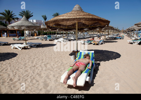 Modell veröffentlicht Mann auf Sommerurlaub und Sonnenbaden auf einer Sonnenliege am Strand mit Sonnenschirme und Großschirme Stockfoto