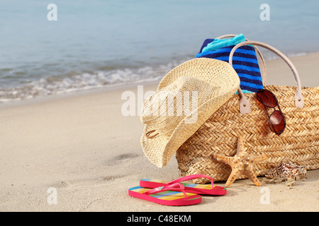 Sommer Strand-Tasche mit Strohhut, Handtuch, Sonnenbrille und Flip Flops am Sandstrand Stockfoto