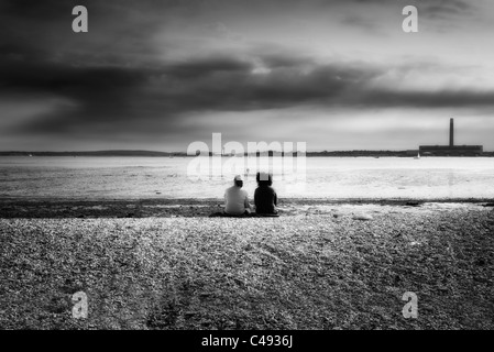 Leute sitzen auf einem Kiesstrand bei Ebbe am Southampton Wasser UK schwarz & weiß Stockfoto