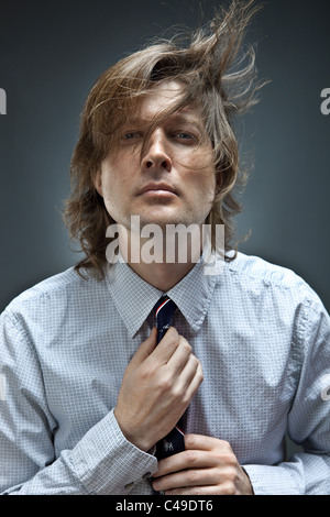 Studioaufnahme des Mannes in Button-Down-Oxford-Hemd passt seine Krawatte, während seine braunen Haare herum bläst. Stockfoto
