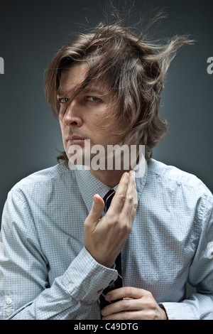 Studioaufnahme des Mannes in Button-Down-Oxford-Hemd passt seine Handfesseln, während seine braunen Haare herum bläst. Stockfoto