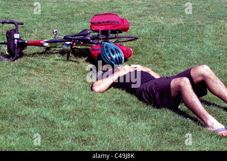 Radfahrer am Rücken in Grass, Mann schlafend am Boden liegen und dabei einfach neben dem Fahrrad Stockfoto
