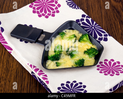 Raclettepfännchen mit Käse und Broccoli auf bunte Serviette Stockfoto