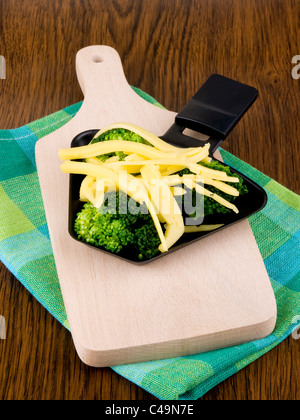 Raclette-Pfanne mit Käse und Brokkoli auf Schneidebrett Stockfoto