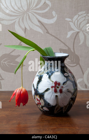 Hängende rote Tulpe in verzierte Vase auf Tischplatte. Stockfoto