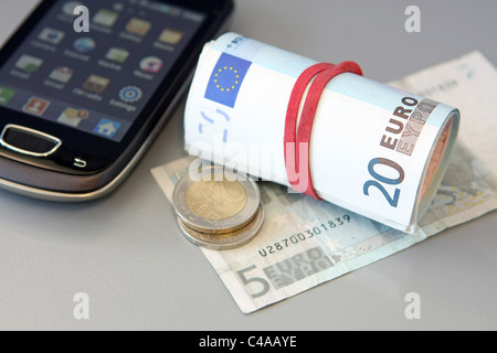 Euro-Münzen und ein Bündel von Euro-Banknoten auf aufgerollt einen 5 Euro-Schein neben einem Mobiltelefon Stockfoto