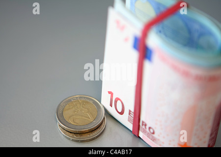 Einige Euro-Münzen neben einem gefalteten Bündel von Euro-Banknoten in einem Gummiband Stockfoto