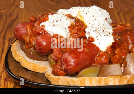 Drei Chili Hunde auf Kartoffeln und Brot, bedeckt in saurer Sahne, Hot Sauce und Pfeffer Stockfoto