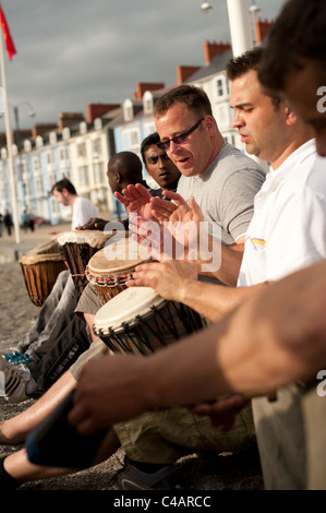 Eine gemischte ethnische Gruppe von Männern, die Teilnahme an eine improvisierte Trommeln Sitzung auf Aberystwyth Promenade, Wales UK Stockfoto