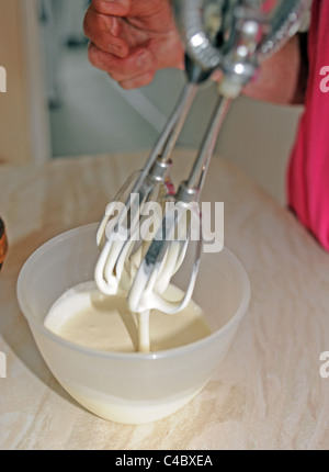 Frau mit einer alten altmodischen Hand Schneebesen in einer Schüssel Sahne in Küche UK Stockfoto