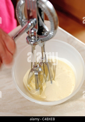 Frau mit einer alten altmodischen Hand Schneebesen in einer Schüssel Sahne in Küche UK Stockfoto