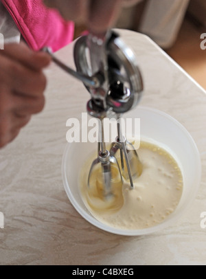 Frau mit einer alten altmodischen Hand Schneebesen in einer Schüssel Sahne in Küche UK Stockfoto