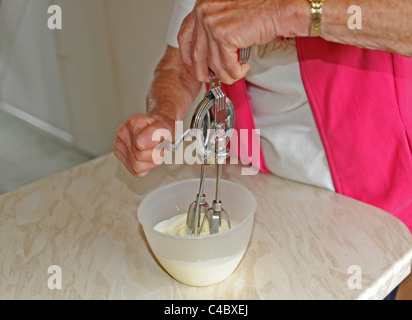 Frau mit einer alten altmodischen Hand Schneebesen in einer Schüssel Sahne in Küche UK Stockfoto